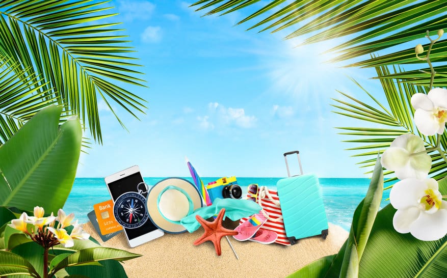 summer tropical background of accessories for travelers on a sandy island surrounded by tropical palm leaves and flowers.